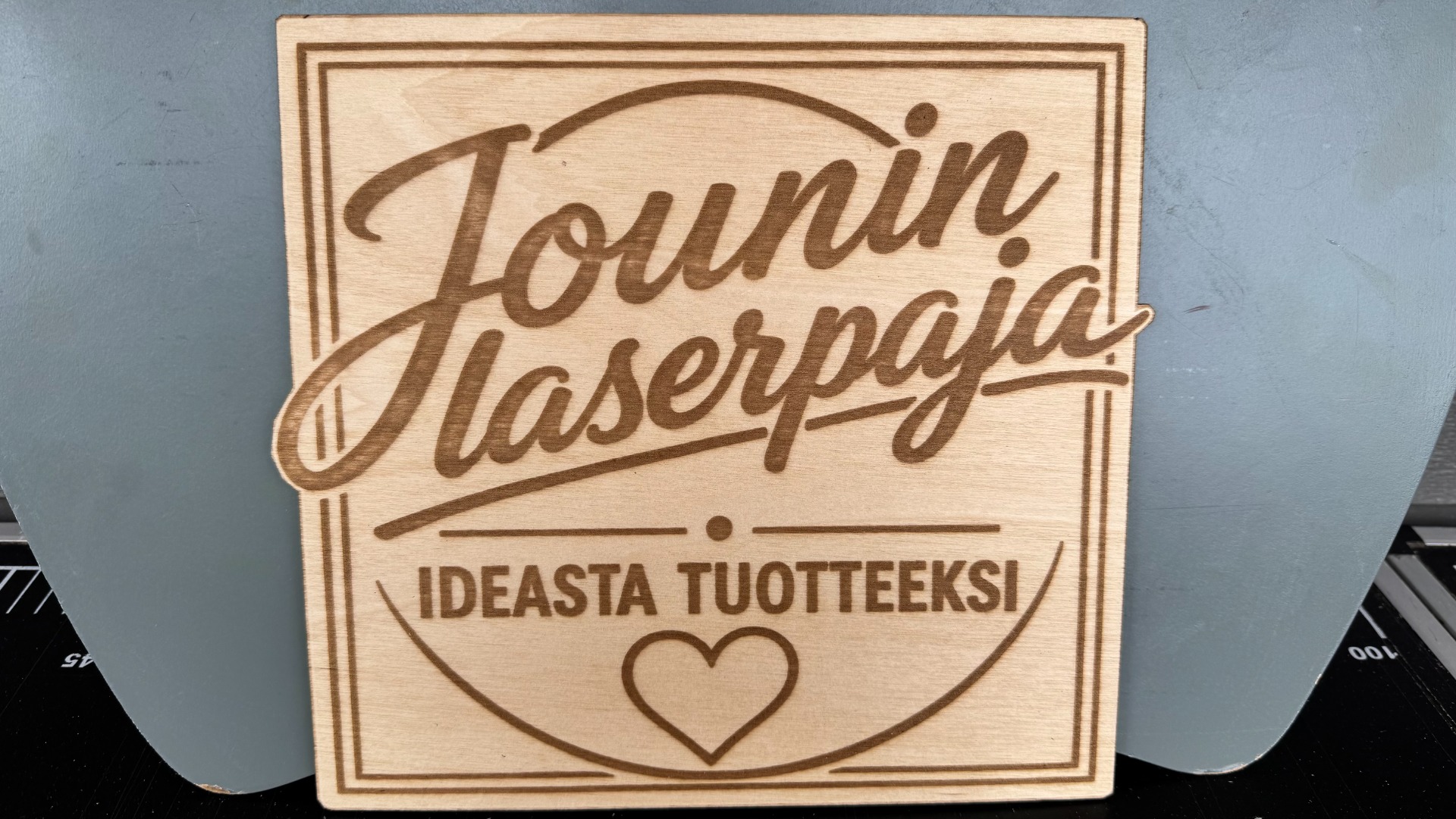 Valkoinen puinen koriste, jossa vihreä puu ja juuret, seisoo puisella jalustalla harmaata taustaa vasten.